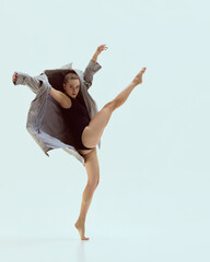 Contemporary dancer kicking high in bodysuit and oversized coat with fierce dramatic gaze. Concept...