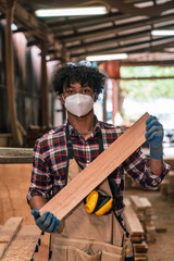 Portrait Of Young African American Carpenter Holding Wood Plank In Timber Workshop, Wearing Apron...