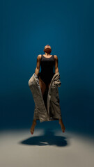 Center stage. Contemporary dancer captured mid-jump under spotlight with coat and lifted face in...