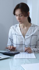 Female professional calculating finances, reviewing paperwork, tracking business expenses with...