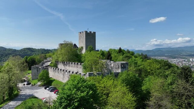 Aerial views of Slovenian landscapes in spring. Drone footage of Celje and its fortress. Historic Celje Castle overlooks vibrant spring townscape, combining medieval legacy and modern life.
