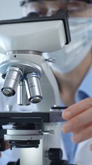 Female scientist wearing lab coat and protective glasses using a modern microscope in a laboratory setting, conducting research and experiments, close up. Health care, medicine and science concept