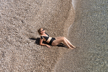 Woman relaxing on a pebbled beach, enjoying the warm sun and gentle waves, embodying the essence of...