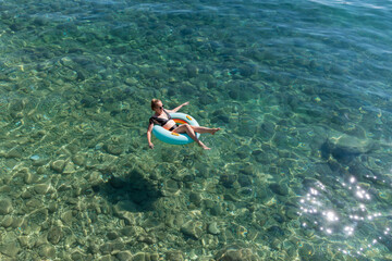 Child is relaxing on a colorful inflatable ring while floating in clear turquoise water, enjoying a...
