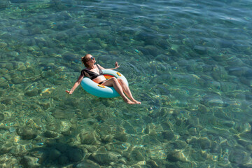Woman relaxing on a floating ring in clear turquoise water, enjoying a sunny day, surrounded by...