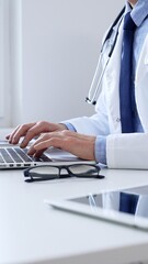 Doctor man typing on laptop, updating electronic patient records with focused concentration, representing digital transformation in healthcare workplace. Medicine and health care