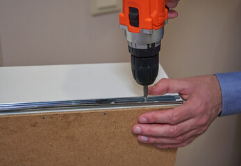 cordless screwdriver tightening guides in furniture, locksmith with the help of a screwdriver installs the mechanism of guides on a drawer, the process of assembling furniture