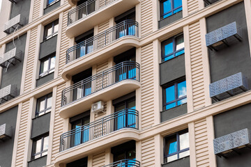 A modern apartment building with balconies, metal railings, air conditioners and decorative elements. The facade is made in light and dark colors.