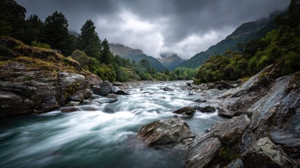 A moody river winds through a valley between lush green hills under a dramatic, cloudy sky