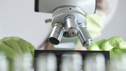 Close up of green gloved hands of a scientist adjusting a microscope in a laboratory, emphasizing the significance of scientific research and analysis. Medicine, healthcare and science concept