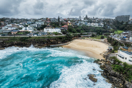 Sydney, Australia - 20 May 2025: Aerial view of turquoise waves crashing against the rugged coastline near Tamarama Beach, nestled beneath the urban landscape.