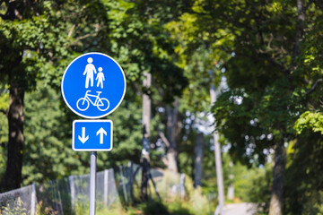 Close-up of a Finnish Traffic Sign for a Shared Pedestrian and Bicycle Path Against a Blurred Green Forest Background