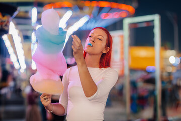 Redhead woman eating cotton candy at amusement park by night