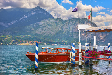 Bellagio, Lake Como, Italy. Water taxi boat by the pear. Mountains and lake on background. Sunny panoramic view. Popular summer vacation travel destination.