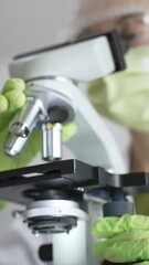 Close up of green gloved hands of a scientist adjusting a microscope in a laboratory, emphasizing the significance of scientific research and analysis. Medicine, healthcare and science concept