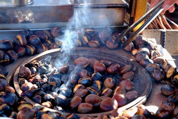 Chestnuts, a traditional Turkish street food. A close-up of a hand holding a chestnut with tongs. Smoke rises as the chestnuts roast over a charcoal fire. Winter.
