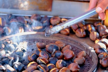 Chestnuts, a traditional Turkish street food. A close-up of a hand holding a chestnut with tongs. Smoke rises as the chestnuts roast over a charcoal fire. Winter.
