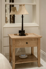 A classic wooden bedside table with a vintage-style lamp and a modern smart home device. Rustic...