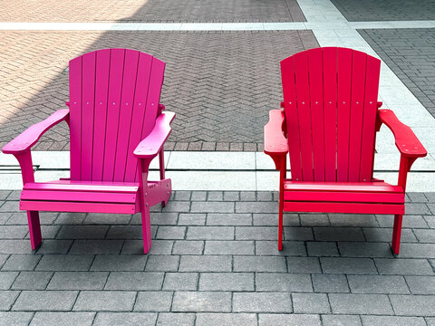 Two colorful wooden chairs pink and red lined up outdoors on a street, creating a vibrant and charming scene perfect for relaxing