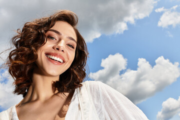 Sunlit beauty with wavy brown hair enjoys a vibrant summer day under a blue sky