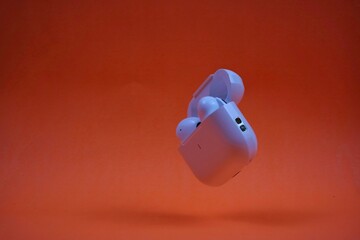 Modern Wireless Earbuds and Charging Case on Bright Orange Background