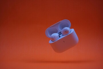 Modern Wireless Earbuds and Charging Case on Bright Orange Background