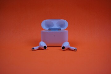 Modern Wireless Earbuds and Charging Case on Bright Orange Background