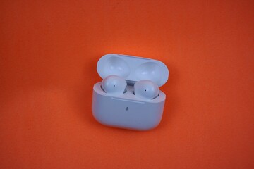 Modern Wireless Earbuds and Charging Case on Bright Orange Background