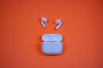 Modern Wireless Earbuds and Charging Case on Bright Orange Background
