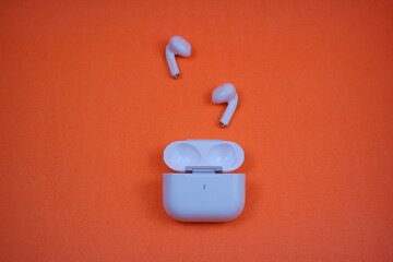 Modern Wireless Earbuds and Charging Case on Bright Orange Background