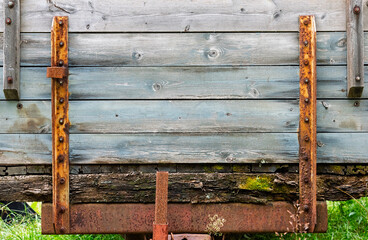 Vintage cart made of weathered wood, secured with rusty metal brackets, surrounded by greenery in a...
