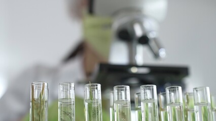 Close up of test tubes with a scientist analyzing plant samples in test tubes with a microscope in...