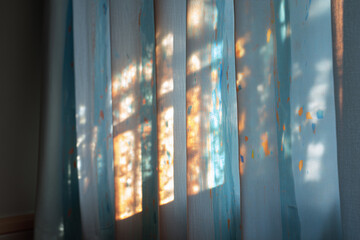 Gently pulled curtain allowing soft light to filter in, casting colorful patterns on the wall during late afternoon hours