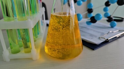 Bright yellow liquid in laboratory flask with test tubes and molecular model nearby during a...