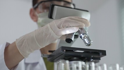 Scientist wearing white gloves adjusting microscope in laboratory setting, conducting scientific research surrounded by test tubes. Medicine, healthcare and science concept