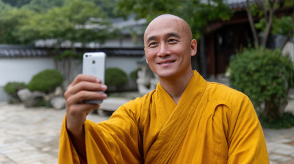 Buddhist monk in traditional robe taking a selfie with smartphone in a peaceful temple courtyard