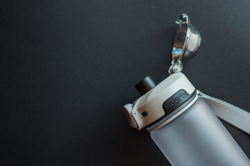 Close-up of frosted sports water bottle with black lid and clear cap on dark background. Minimalist...