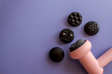 Close-up of a pink massage gun and four black massage heads on a soft purple background....