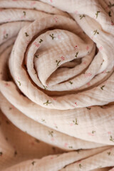 Close-up of soft beige muslin fabric with tiny floral print, artistically rolled into a spiral....