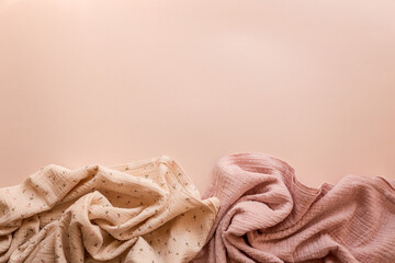 Two soft muslin fabrics in pastel pink and cream with floral patterns arranged on a minimal beige...