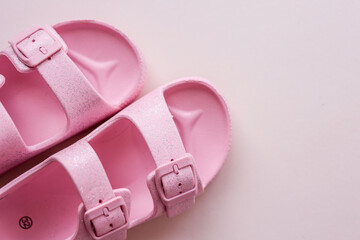 Pair of pink glittery children’s sandals with buckles, arranged diagonally on a soft pastel...