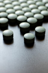 Multiple round black tablets arranged on blue surface. Dietary supplement and pharmaceutical medicine concept. Macro shot photography. 
