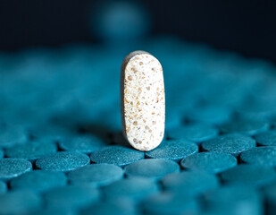 Single speckled beige tablet standing on blue round tablets. Dietary supplement and pharmaceutical medicine concept. Macro shot photography