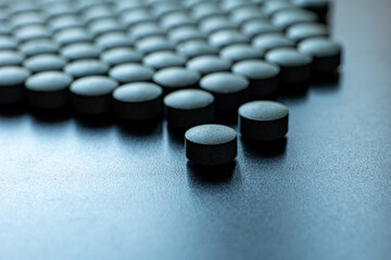 Multiple round black tablets arranged on blue surface. Dietary supplement and pharmaceutical medicine concept. Macro shot photography. 