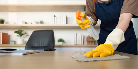 Home Cleaning. Woman using spray bottle to clean a desk in her modern office.