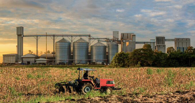 Agricultural Silos - Building Exterior, Storage and drying of grains, wheat, corn, soy, sunflower against the blue sky  with farm tractors in the foreground.