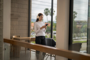 Happy businesswoman enjoying music and using phone app in modern office space