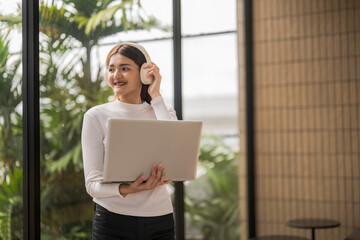 Young asian freelancer listening music with headphones and holding laptop