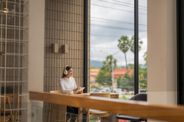 Asian woman enjoying music with headphones and working on a tablet in a cafe