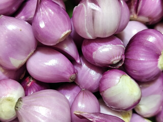 A pile of bright purple fresh shallots with some of the skin peeled off, revealing their natural layered texture, ideal for seasoning dishes.